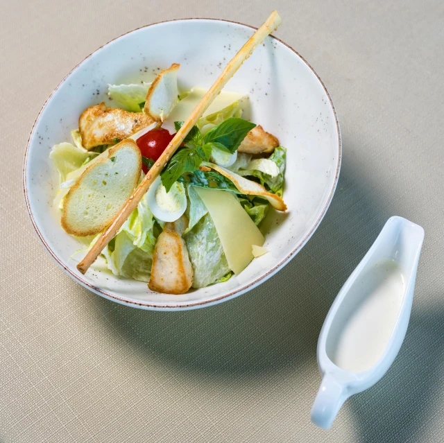 a bowl with a salad inside and another dish with dressing