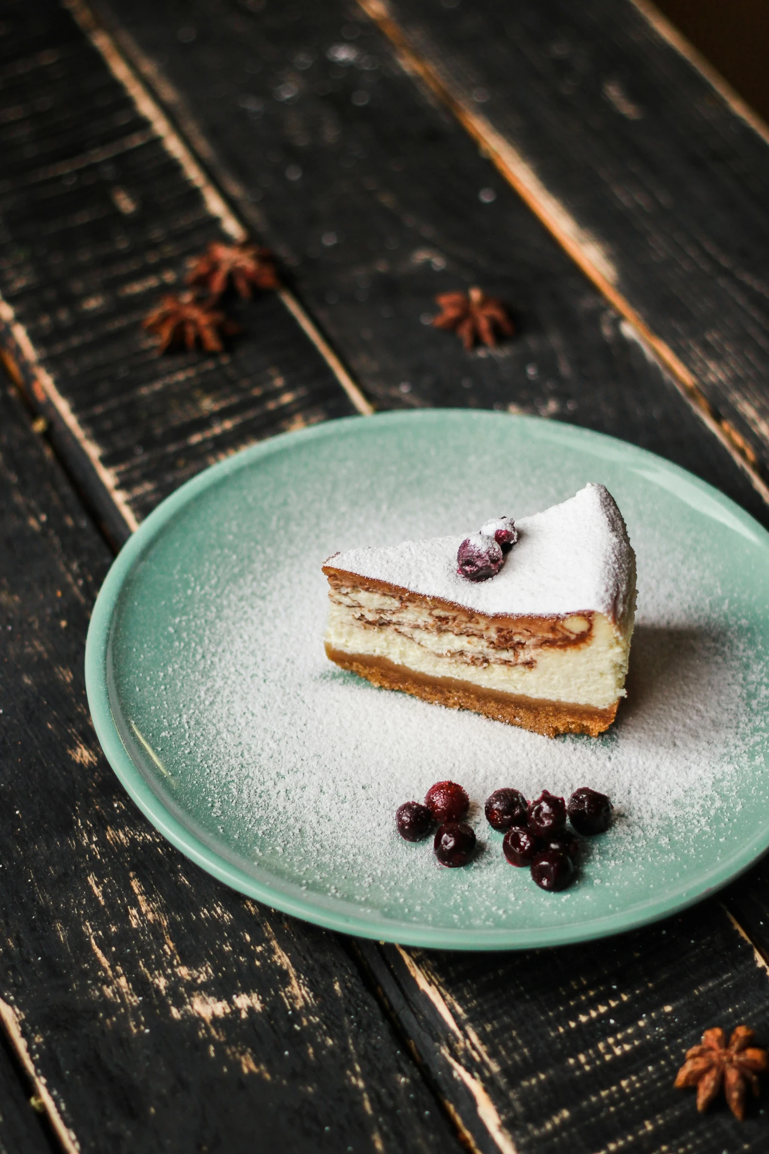 a piece of cake on a plate with blueberries and star anise scattered around