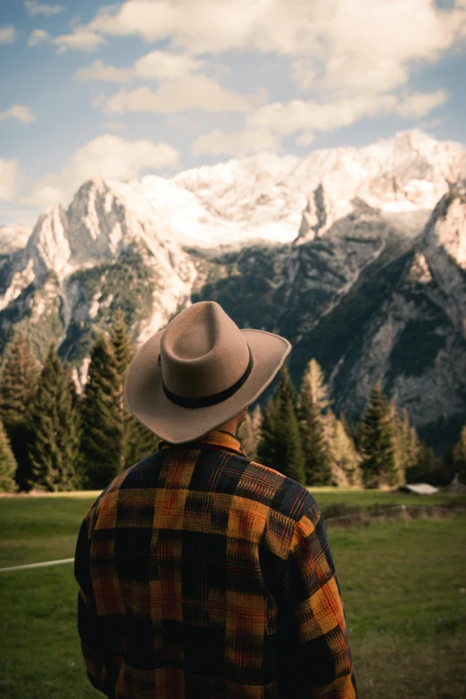 man looking out at mountains and trees from grassy field