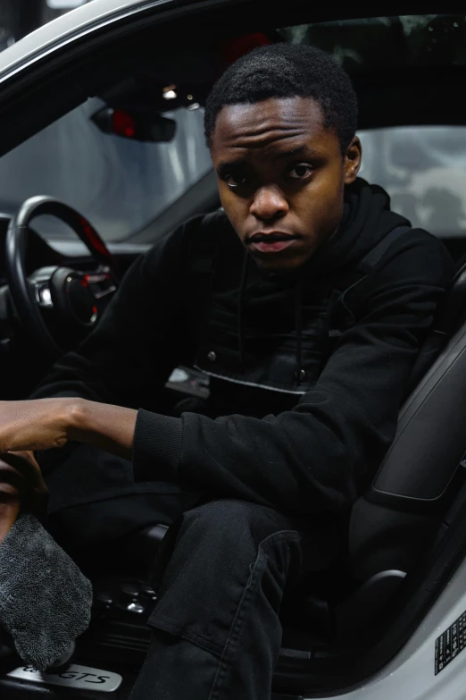 man sitting inside car with black sweatshirt on, hoodie on