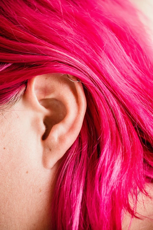 pink haired girl with dark, pale cheeks has her ear clipped back and the back of the ears slightly down