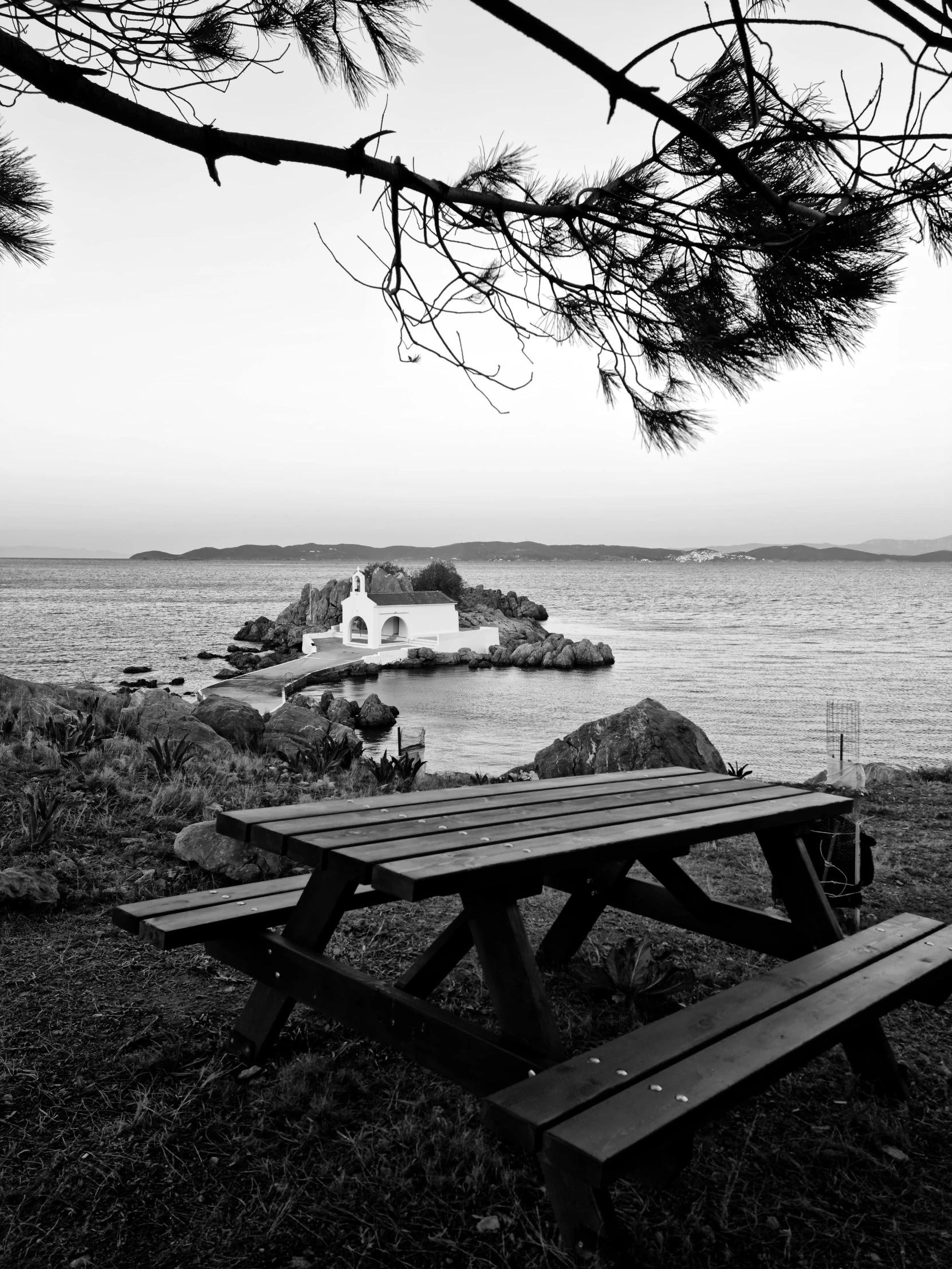 a bench at the shore of the sea is in black and white