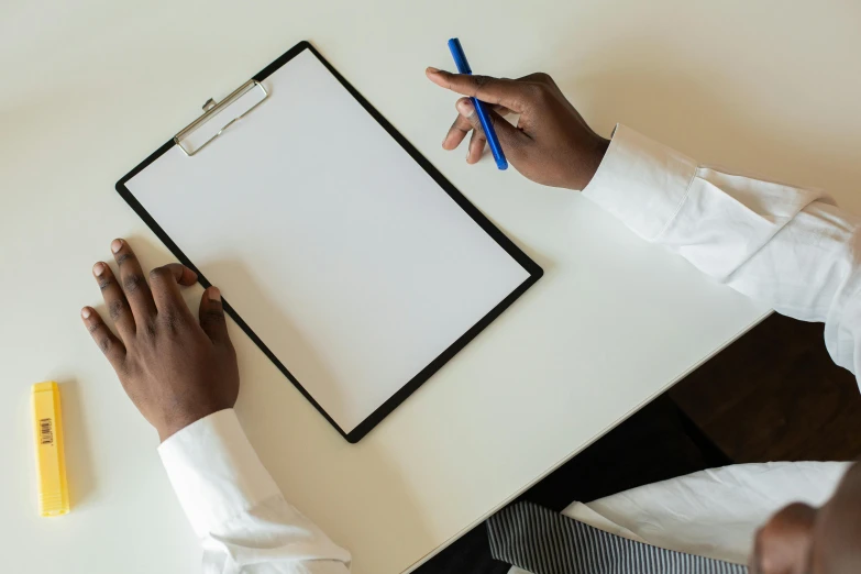 a person in white shirt and blue pencil at table writing