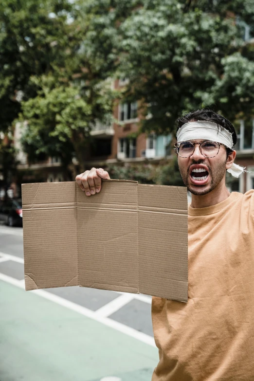 a man is holding up a cardboard box with a sign in front of him