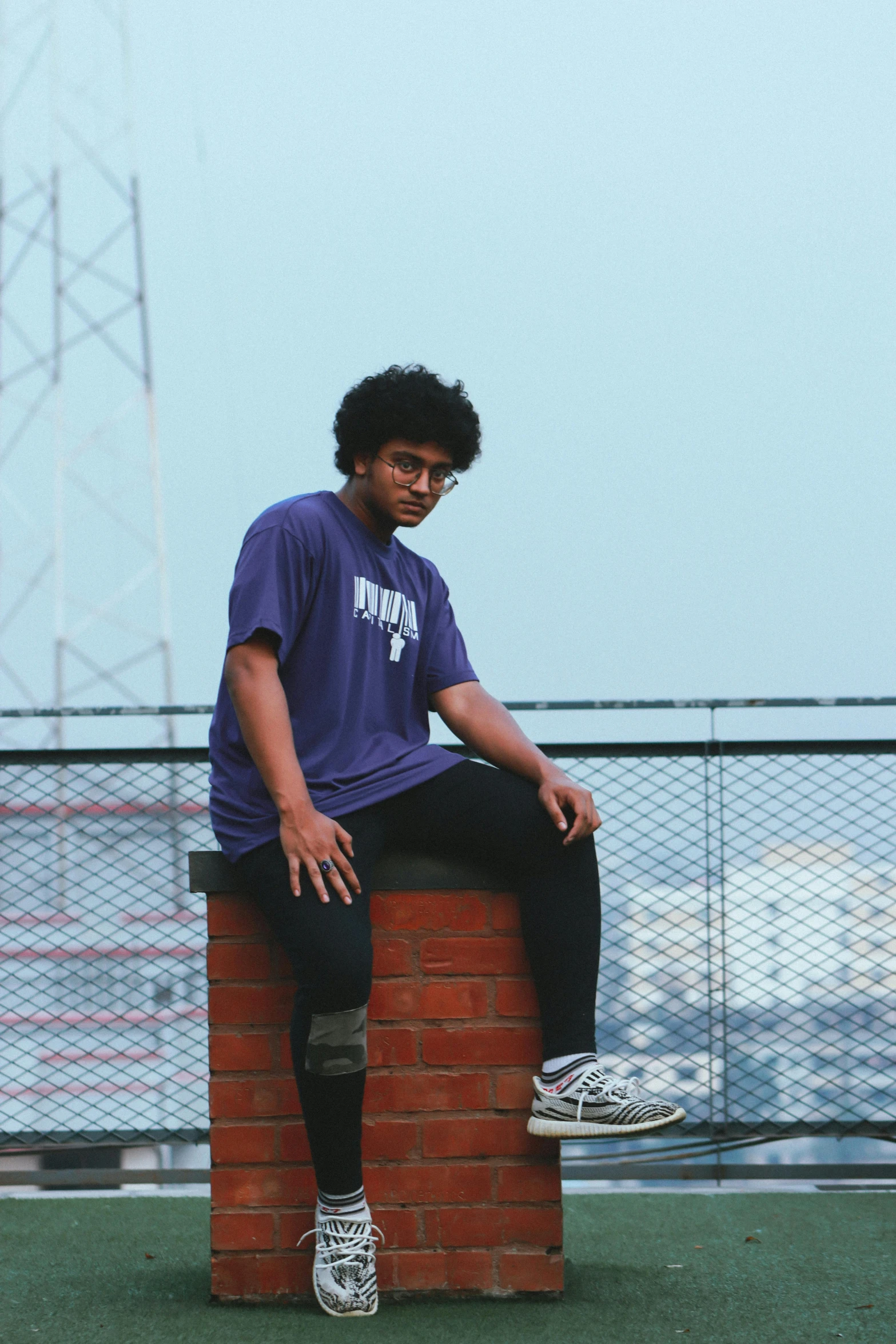 man sitting on brick block next to fence looking off into the distance