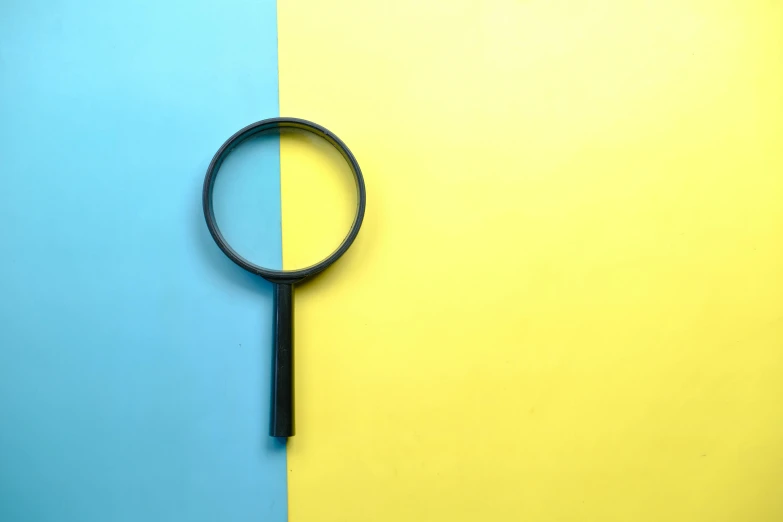 a magnifying glass with a black handle is on a yellow and blue background