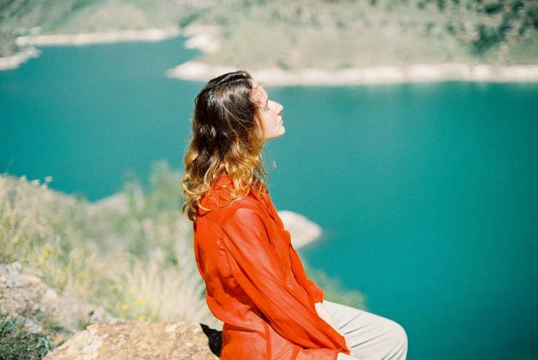 a woman in an orange shirt is sitting on a hill