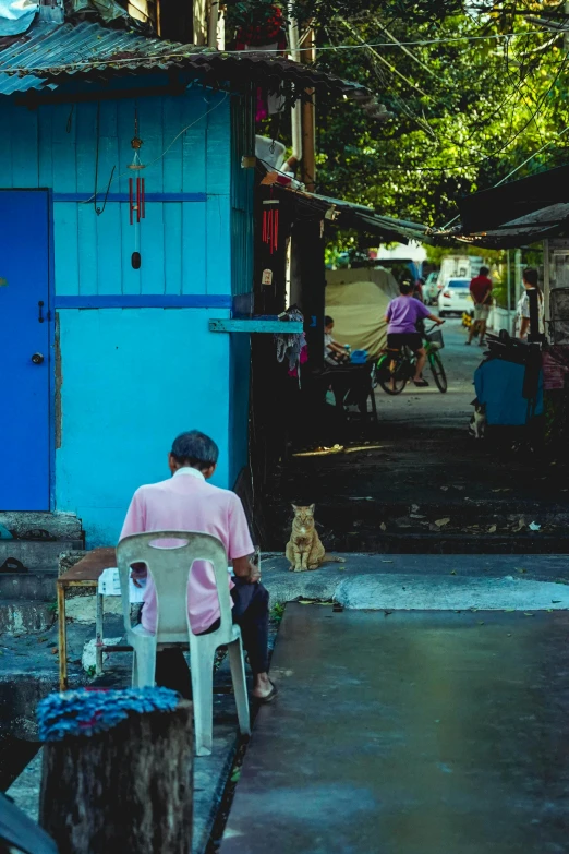 a woman sitting at the end of a porch next to a wooden blue building