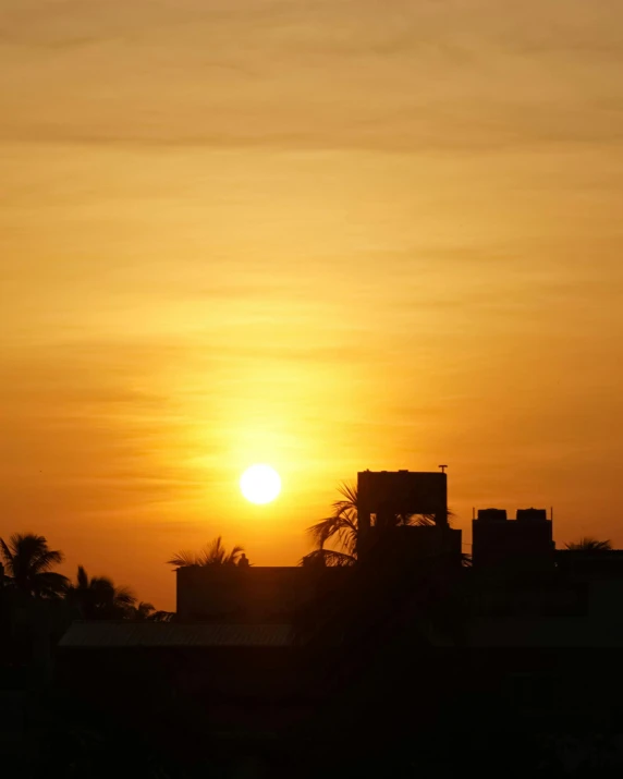 the sun is setting over buildings with trees and palm trees