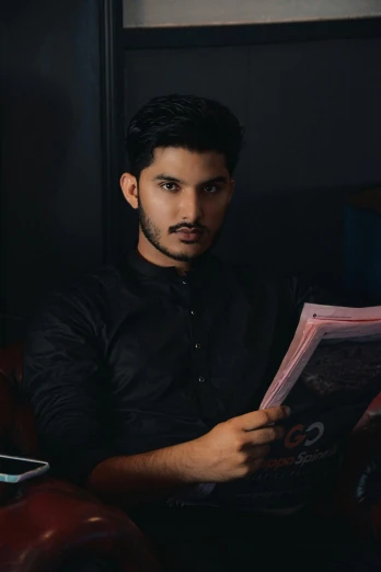young male reading a newspaper with dark lighting