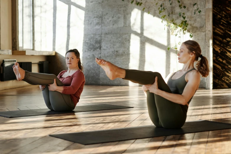 women sit on yoga mats and hold up their legs