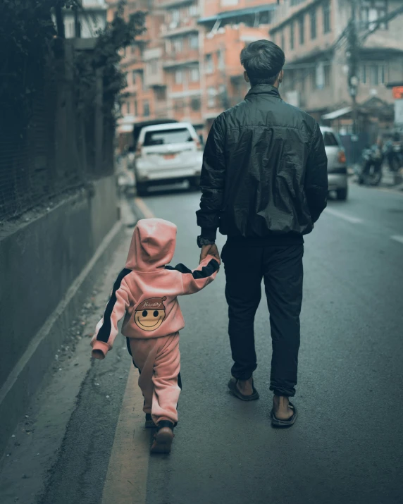 a person walks down a street holding the hand of a child