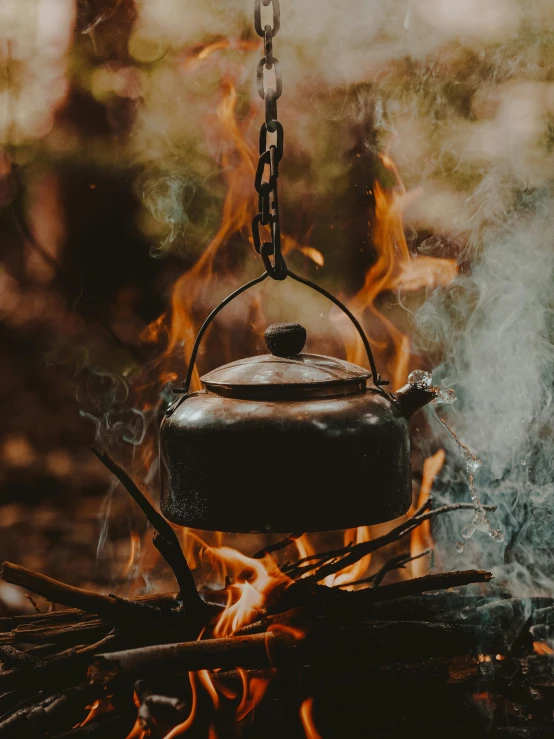 there is a tea pot hanging from the handle over a campfire