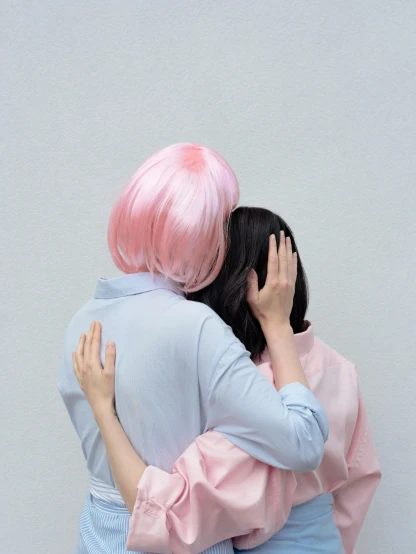 two people with pink hair hugging against a gray wall