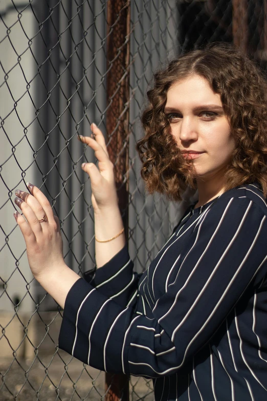 a woman leaning against a fence, with a sad look on her face