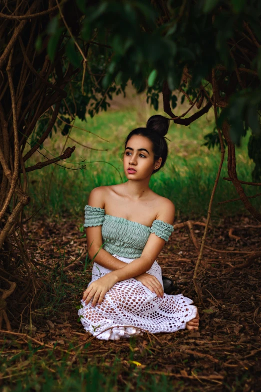 a woman sits on the ground near a tree