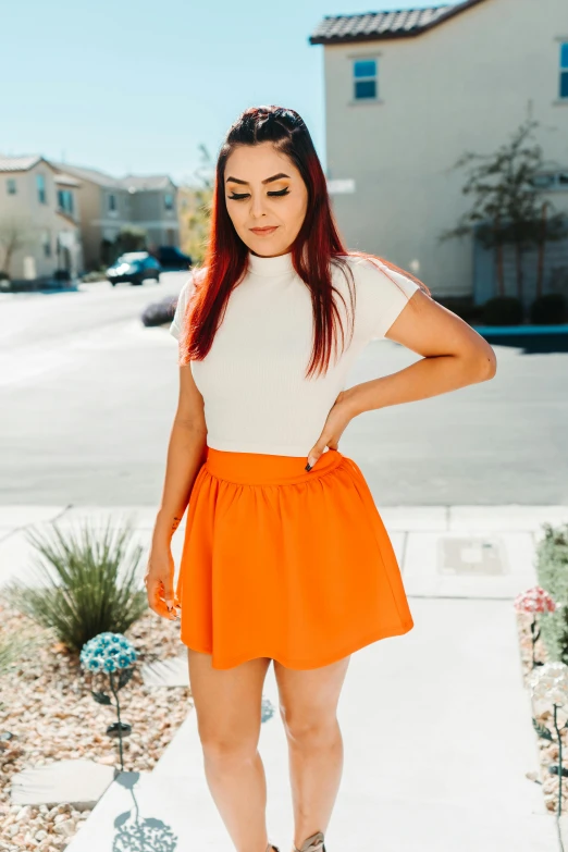 a young woman in an orange skirt and sneakers is posing for the camera