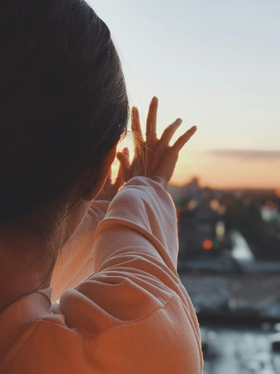 a woman with her hand up and the sun in the background