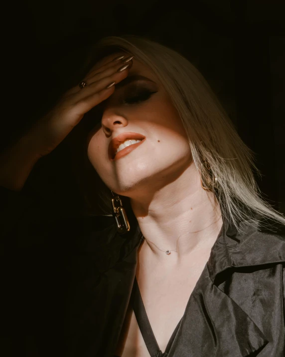 a woman with long blond hair, wearing a black shirt and large earrings