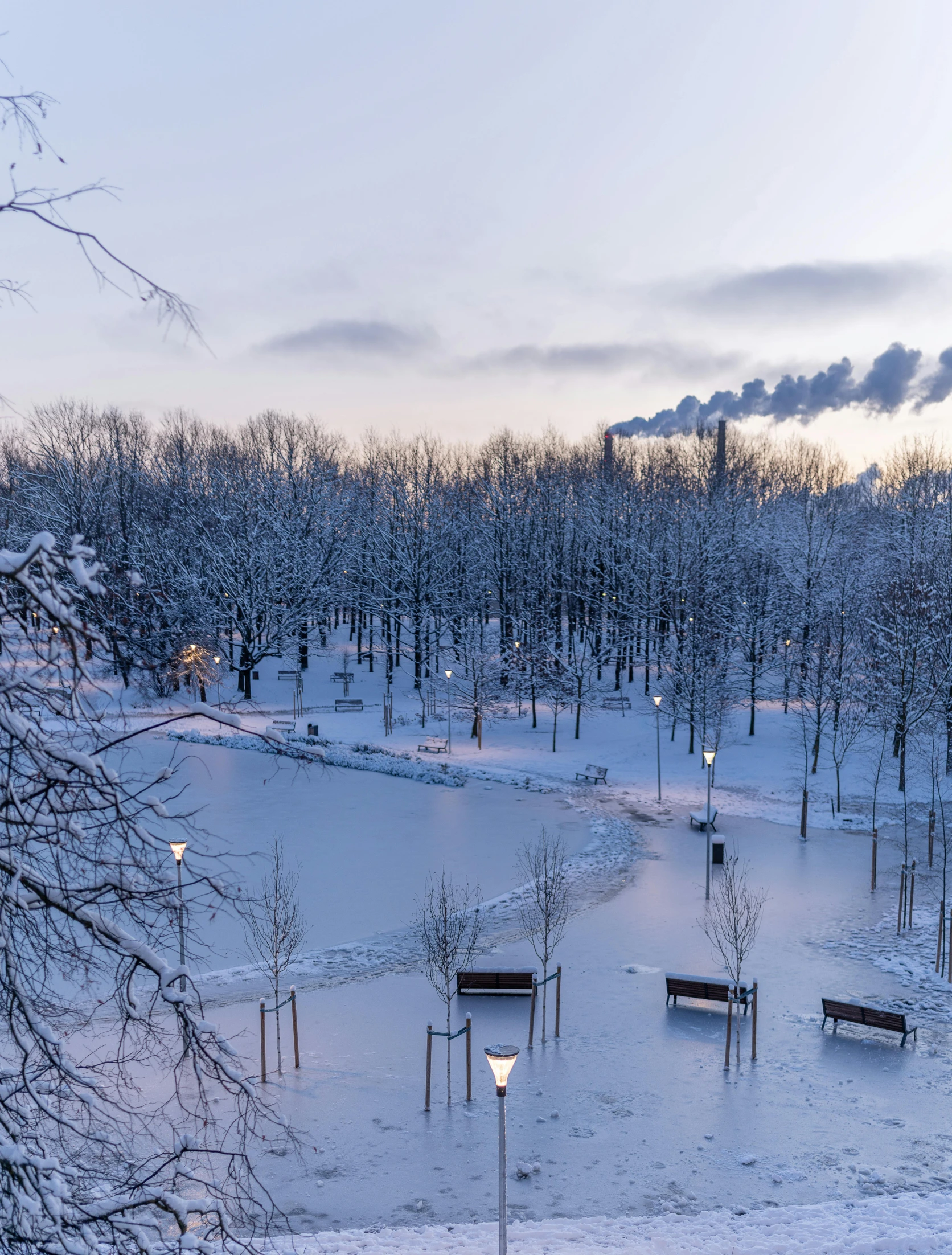 a snowy park at sunset with benches, lanterns and trees