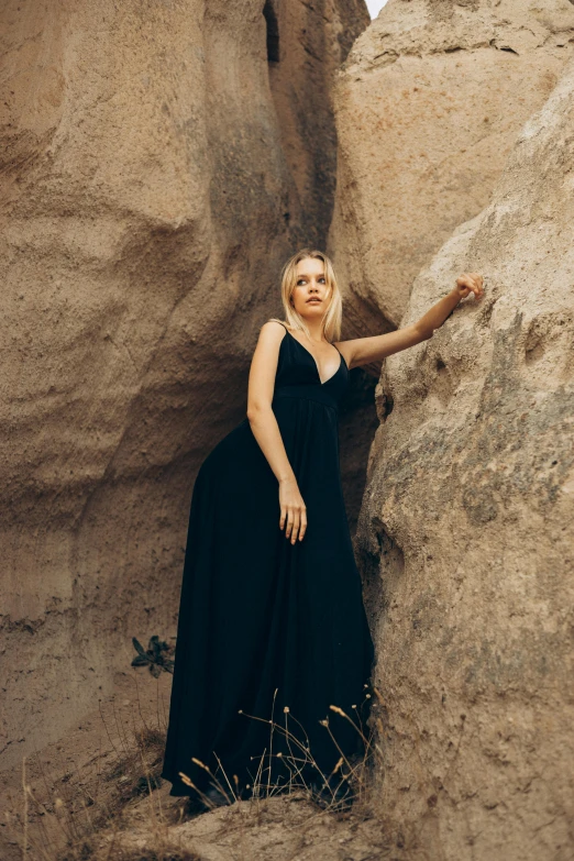 the woman is wearing a black dress standing next to some big rocks