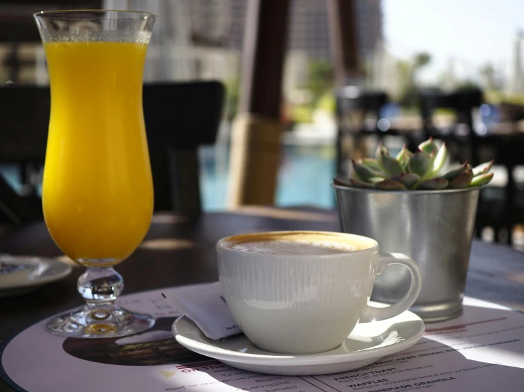 a cup and saucer sit on a table next to a small glass of orange juice