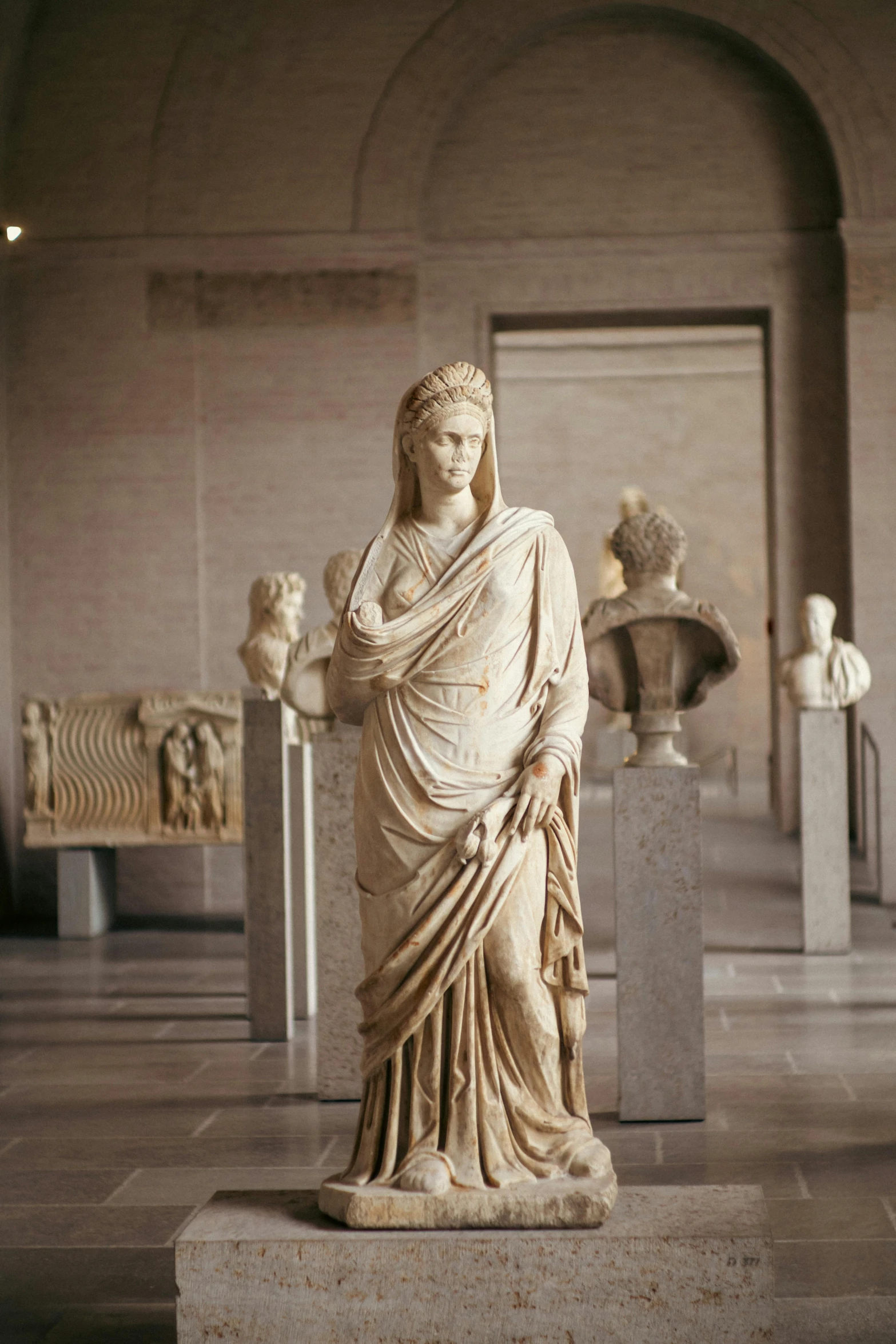 marble statues at a museum with a wall of statues in the background