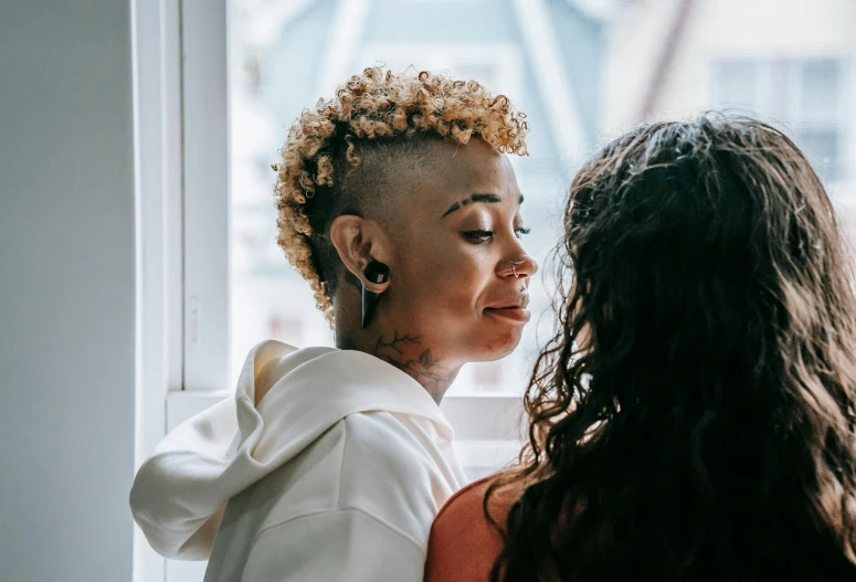 two woman staring out the window, one with brown hair and one without