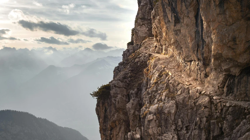 a man walks along the edge of a cliff, with mountains in the background