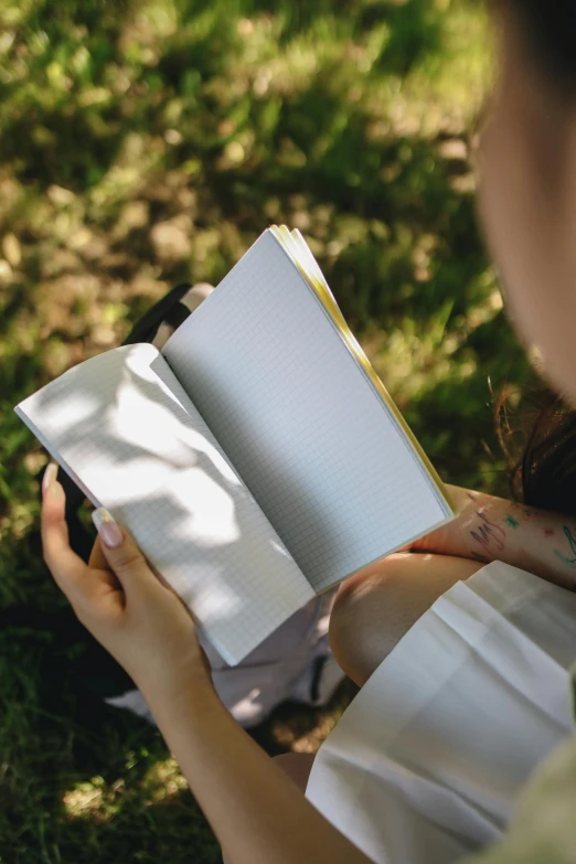 a girl reading an open book while sitting on the grass