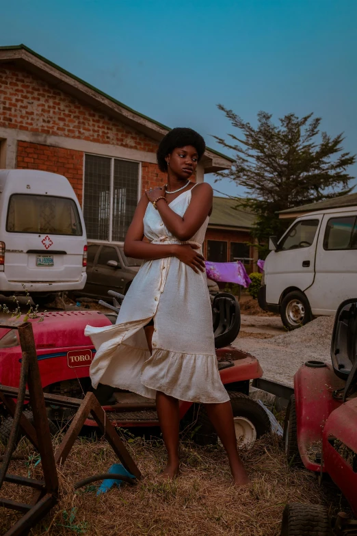 a woman in a white dress standing near a pile of old cars