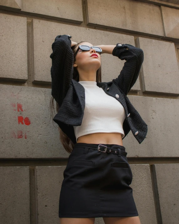 a young woman poses by a brick wall wearing a black skirt and jacket