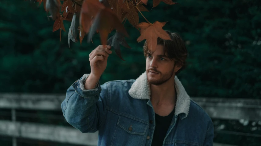 a man standing under an umbrella holding onto leaves