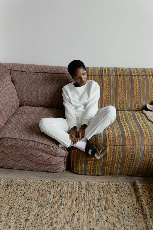 a woman sitting on the couch wearing white and using a phone