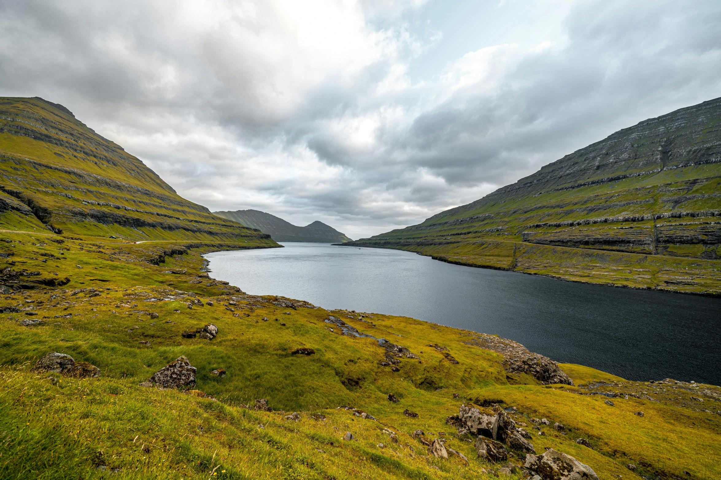 water sitting between two mountains on top of a green grass field