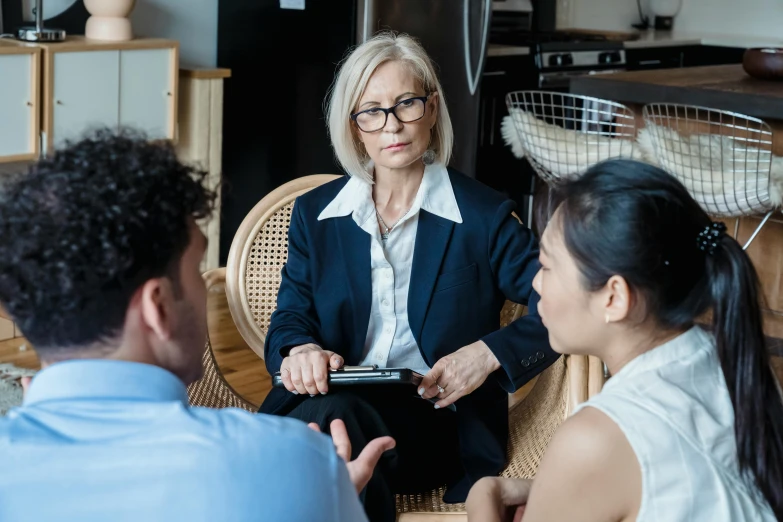 a woman in glasses sits at a table with other people