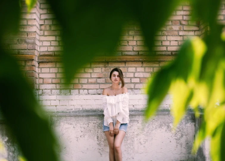 a woman posing in shorts and a white blouse with a plant in the background