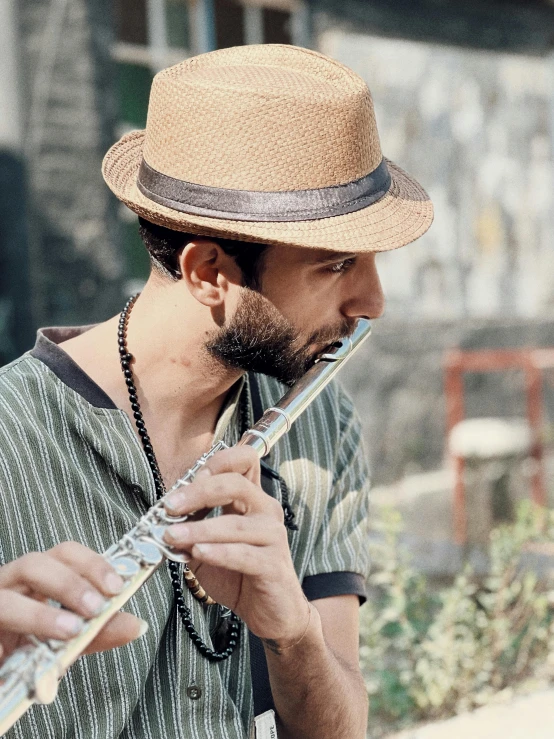 a man in a fedora plays an instrument outside
