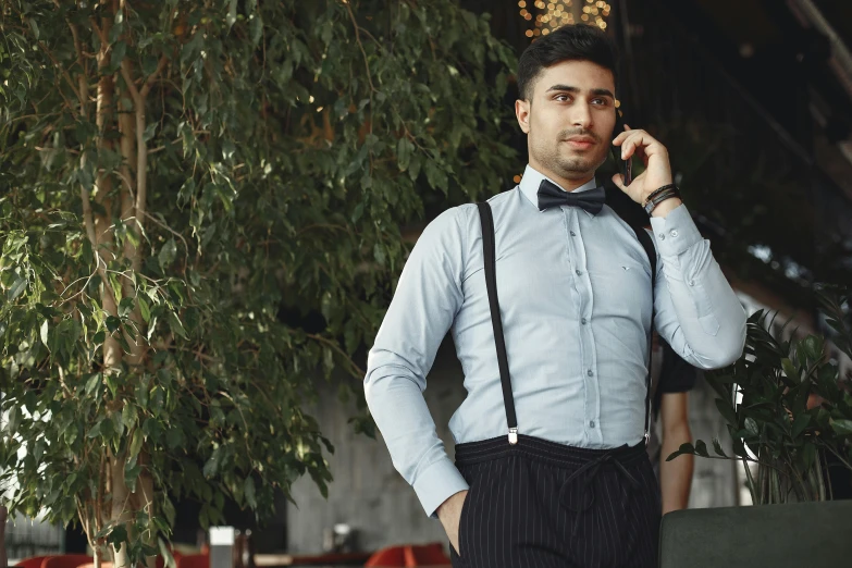 a man in black pants and bow tie is talking on his cellphone