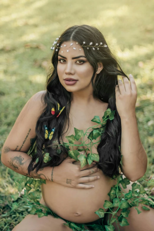 a young belly - baring woman with green foliage around her bust