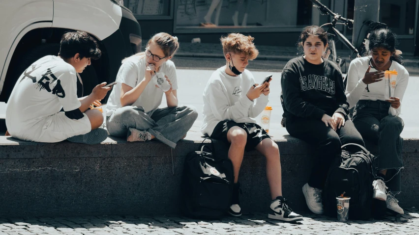 five people sitting on the curb with their mobile devices