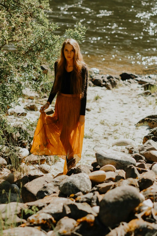 a woman is walking down the beach carrying her orange dress