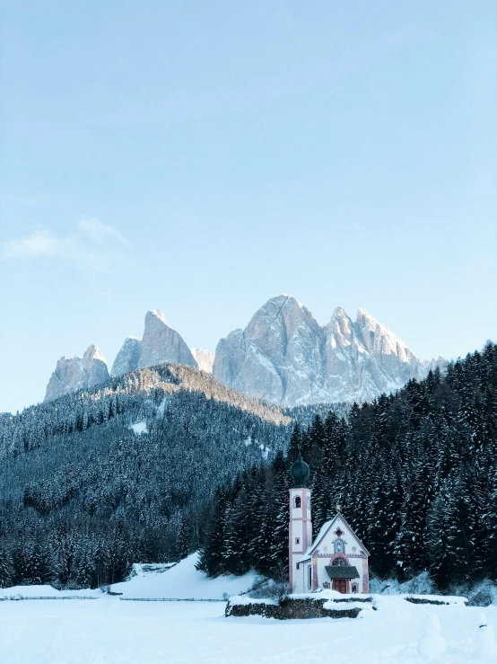 a snowy hill with a house in the foreground and mountains in the background