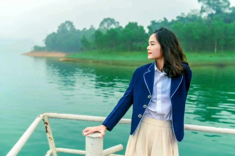 a young woman in a blue jacket leaning against a railing looking at water