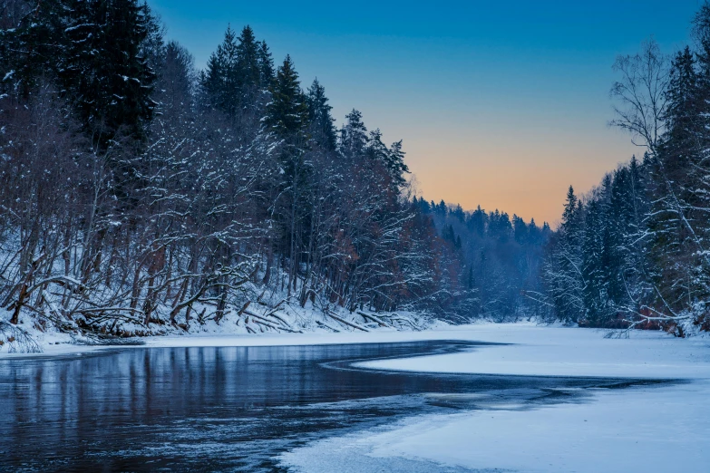 an icy river with snow around trees and the setting sun