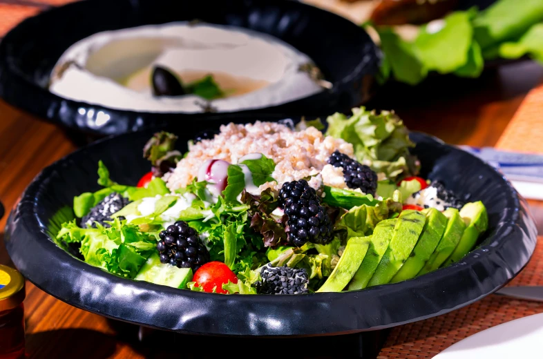 a bowl filled with salad and blackberries next to a table