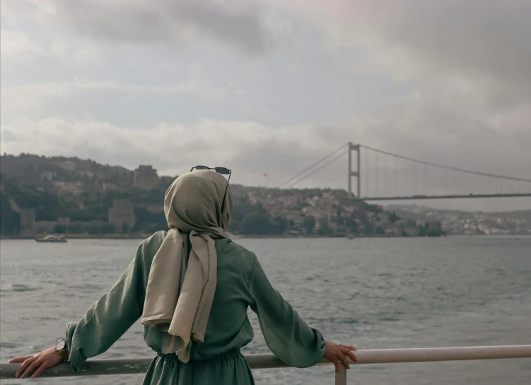 a woman looking out at the ocean by a suspension bridge