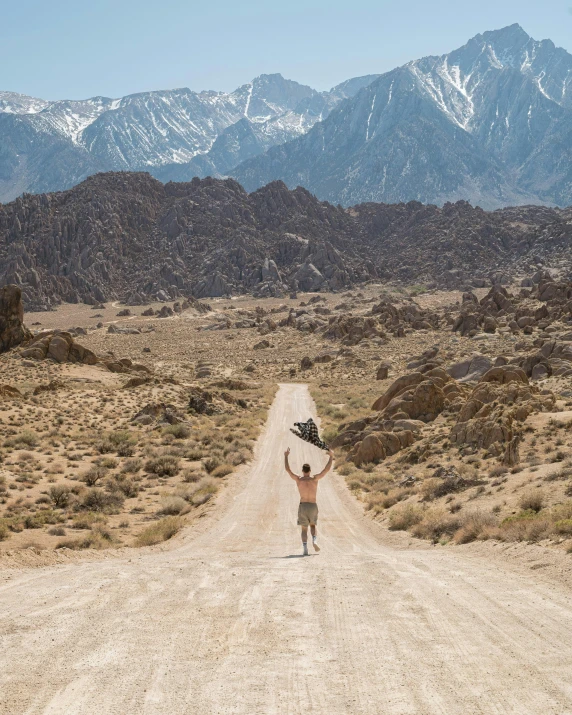 a man standing on a dirt road near mountains