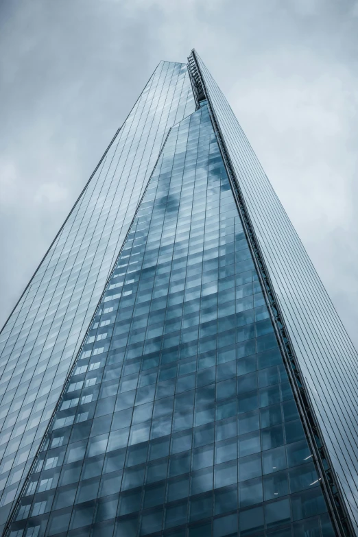 a tall glass and steel building with clouds passing by