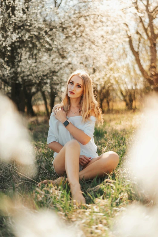 a beautiful young woman is sitting in the grass with her hands under her chest